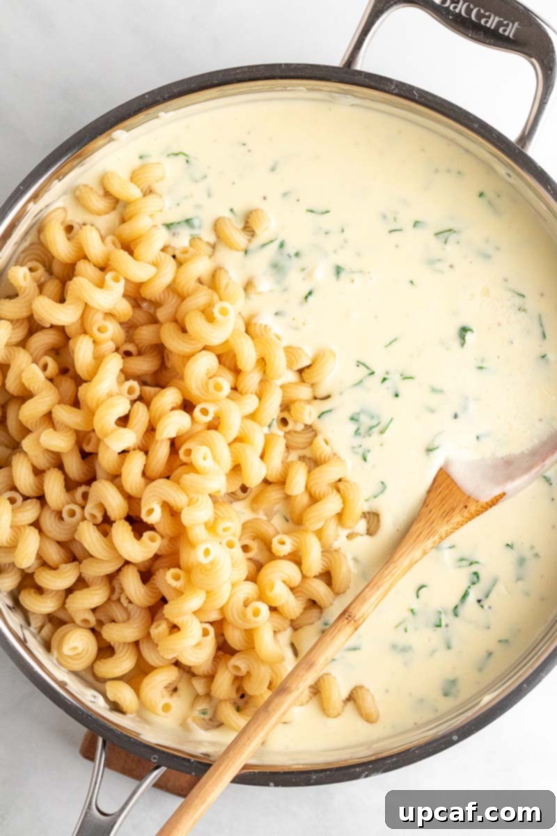 Cooked pasta being stirred into the creamy spinach cheese sauce in a large skillet.