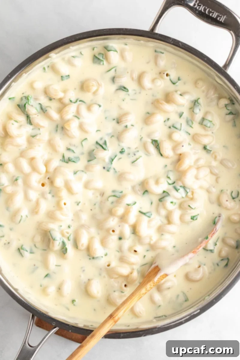 A serving of creamy spinach mac and cheese in a skillet with a wooden spoon, ready to be dished out.