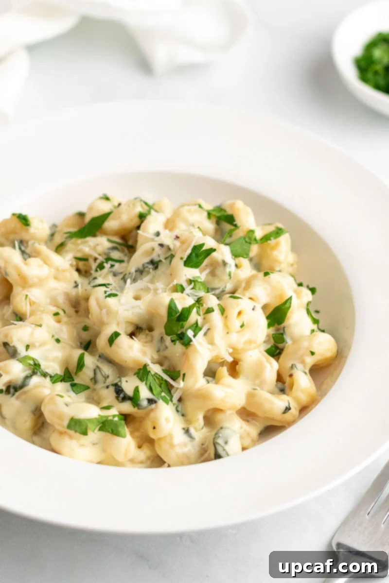 A serving of creamy spinach mac and cheese on a white plate, garnished with fresh parsley and a sprinkle of Parmesan.