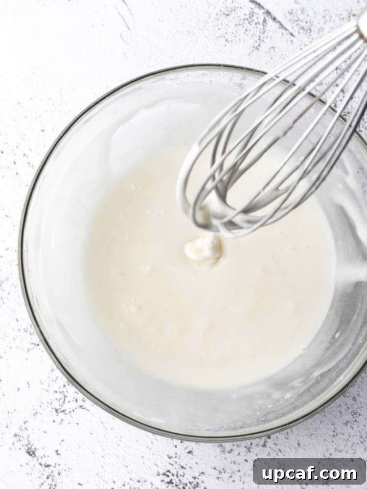 Tangy Lemon Glazed Shortbread 8 Close-up shot of a bowl of freshly whisked lemon sugar icing, smooth and glossy, with a whisk resting inside, indicating its readiness for cookie decorating.