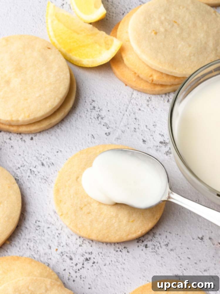 Tangy Lemon Glazed Shortbread 9 A hand gently spoons lemon icing onto the center of a baked shortbread cookie, illustrating the spreading method for decorating, with more cookies in the background awaiting their turn.