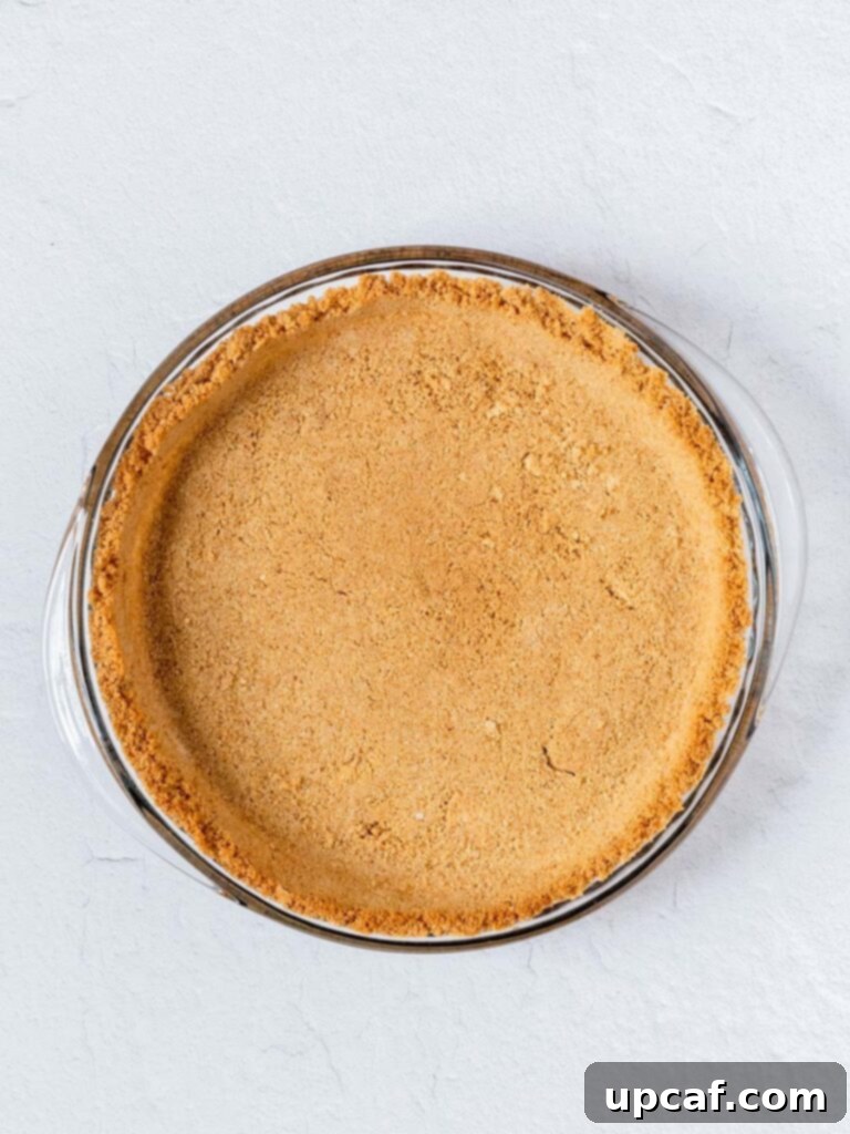 A freshly baked golden brown graham cracker pie crust resting in a pie dish, cooling after coming out of the oven.