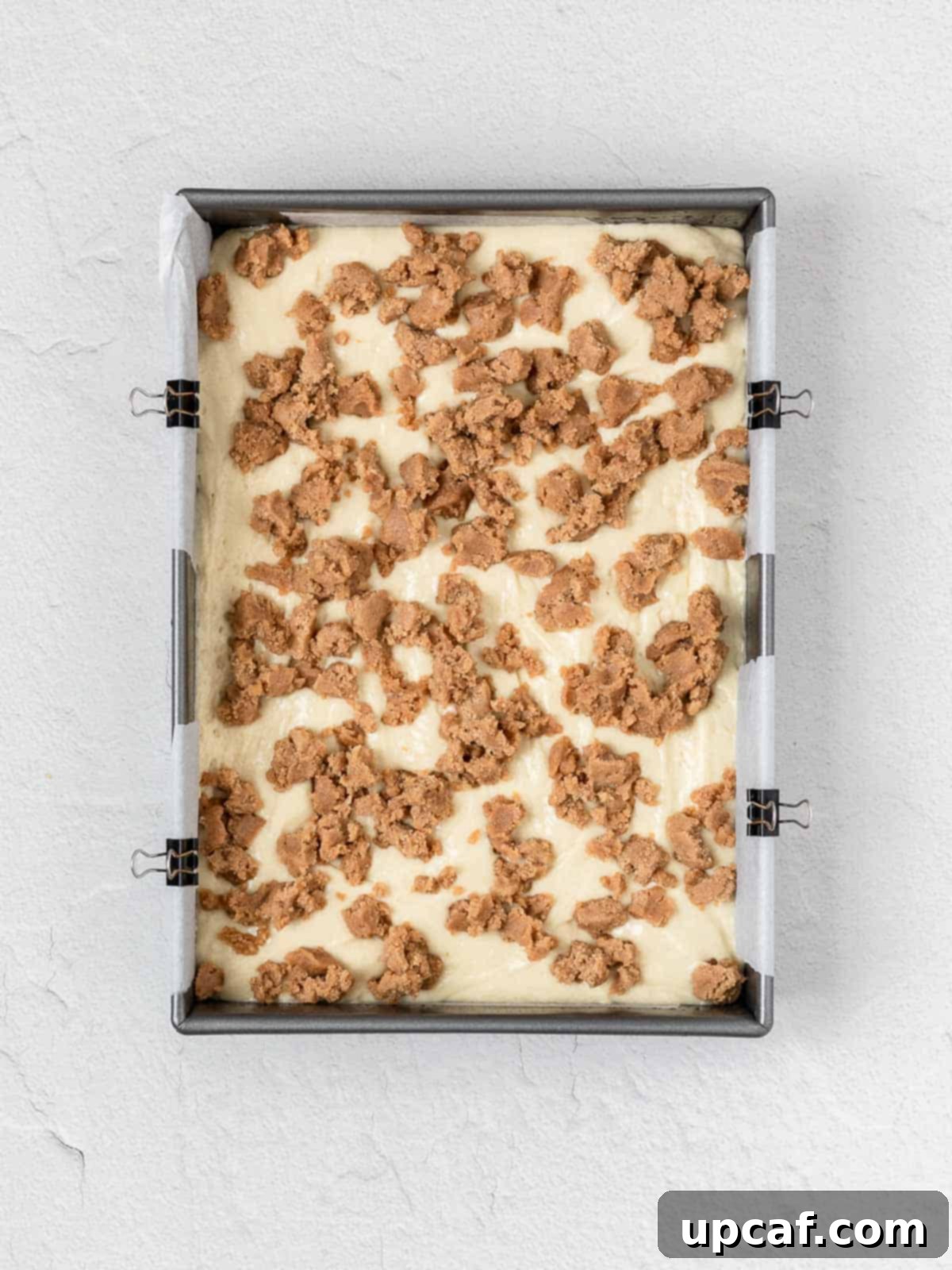 uncooked cake batter in a pan topped with streusels, ready for the oven