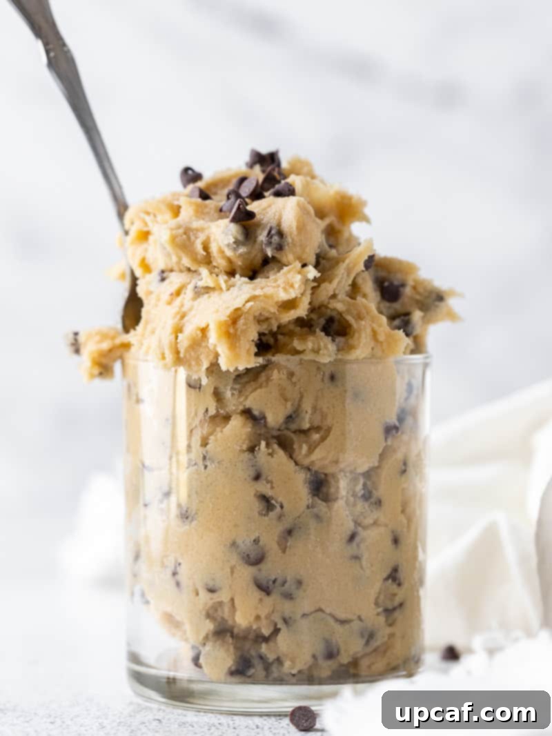 Irresistible Eggless Cookie Dough 2 A clear glass filled with homemade edible cookie dough, with a spoon resting inside, ready to be enjoyed.