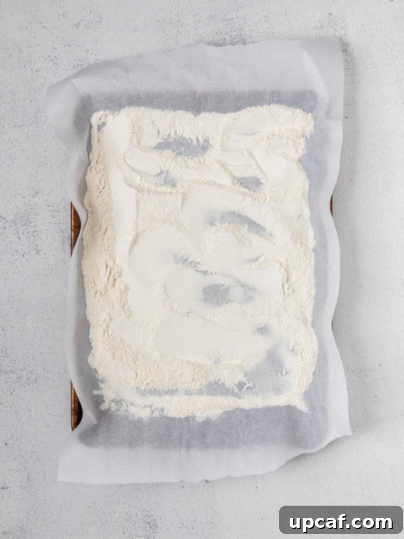 Irresistible Eggless Cookie Dough 4 All-purpose flour spread evenly on a parchment-lined baking sheet, ready for heat treatment in the oven.