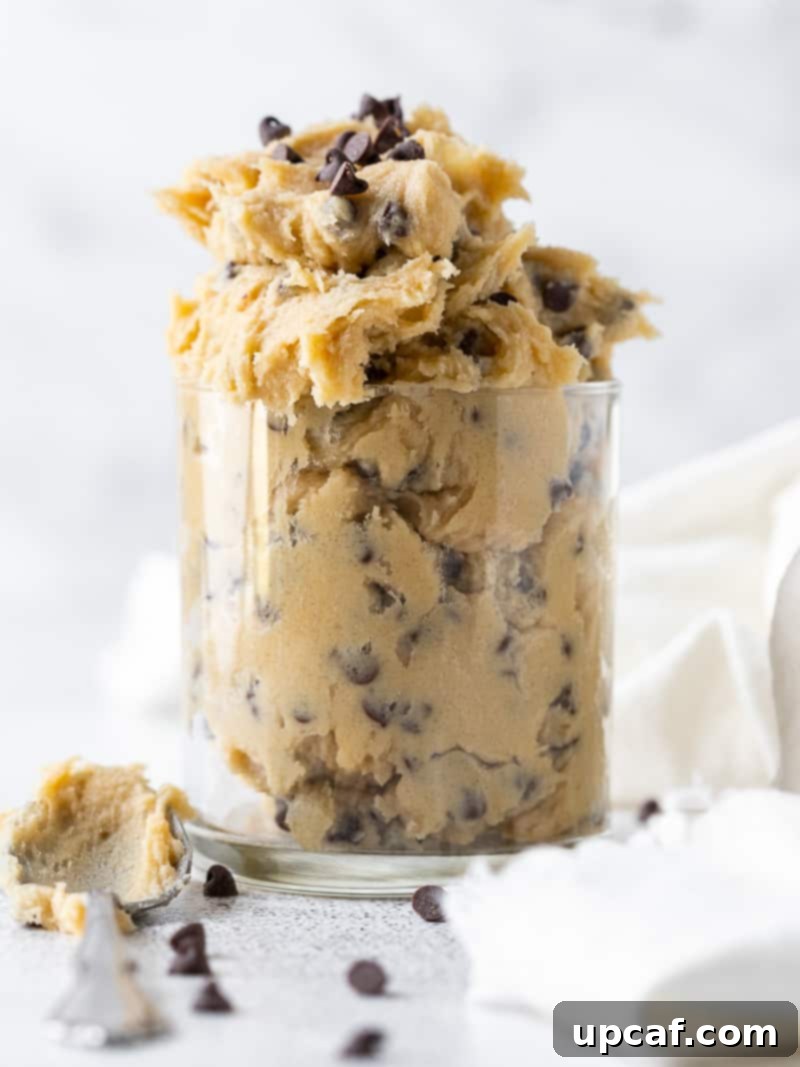 Irresistible Eggless Cookie Dough 7 A beautifully clear glass filled to the brim with creamy, chocolate-chip studded edible cookie dough, ready for enjoyment.