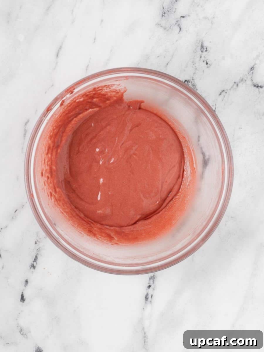 The red velvet macaron batter in a bowl, showcasing its ideal consistency—smooth, flowing, and ready for piping, reflecting the successful macaronage stage.