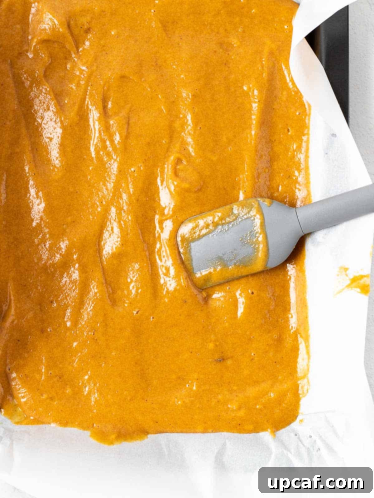 pumpkin cake batter smoothly spread on a parchment-lined baking pan