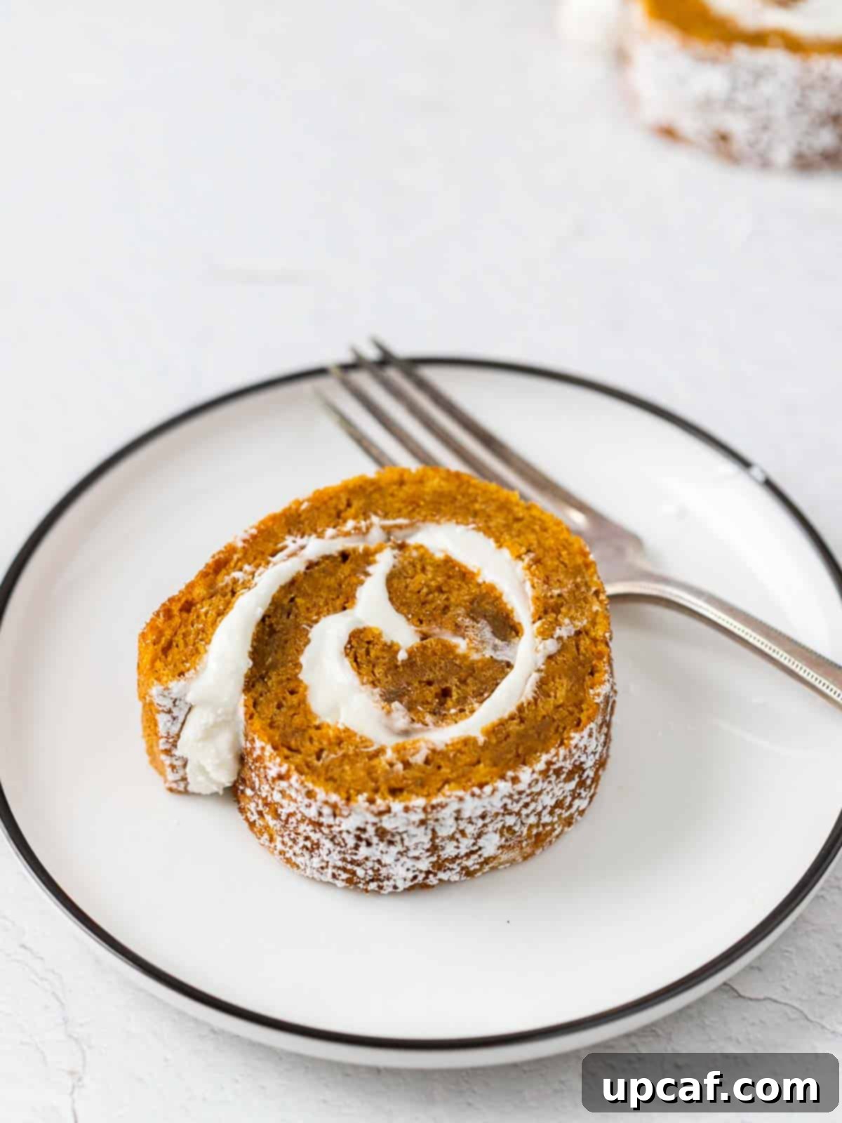a perfect slice of pumpkin cake roll on a white plate, accompanied by a fork