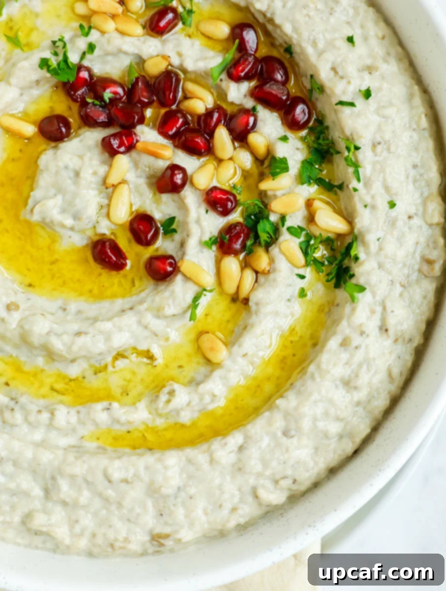 Smoky Lebanese Baba Ganoush 12 A vibrant close-up of Baba Ganoush in a bowl, showcasing its rich texture and colorful garnishes of toasted pine nuts, fresh parsley, and bright pomegranate seeds, inviting viewers to taste.