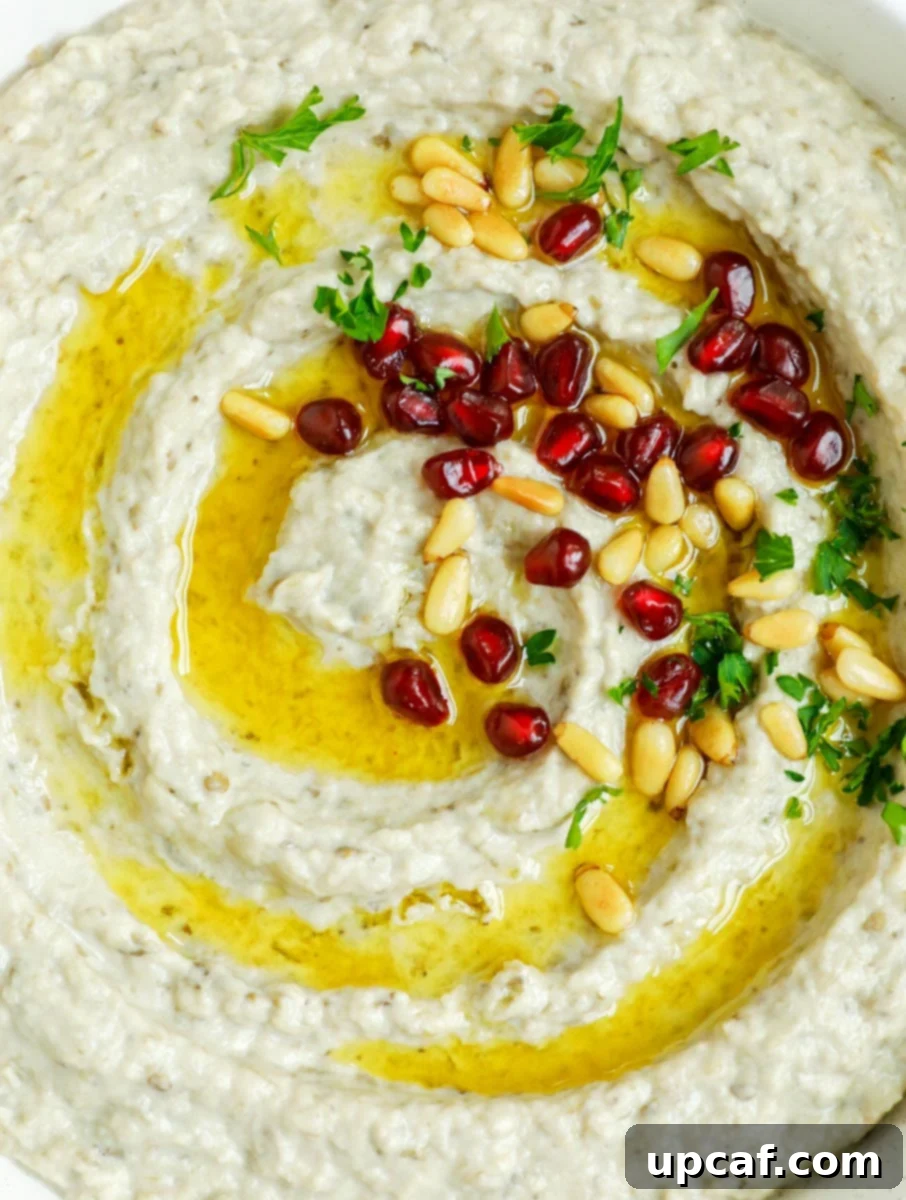 Smoky Lebanese Baba Ganoush 8 A beautifully presented dish of Baba Ganoush, artfully topped with golden toasted pine nuts, fresh green parsley, and sparkling ruby pomegranate seeds, all drizzled with olive oil.