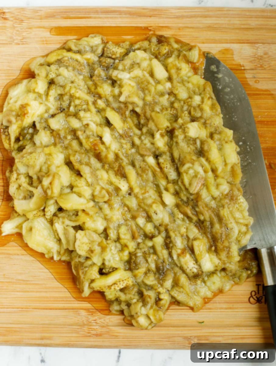 Smoky Lebanese Baba Ganoush 9 A close-up shot of roasted eggplant flesh being finely chopped on a cutting board with a knife, illustrating the traditional method of preparing Baba Ganoush without blending.