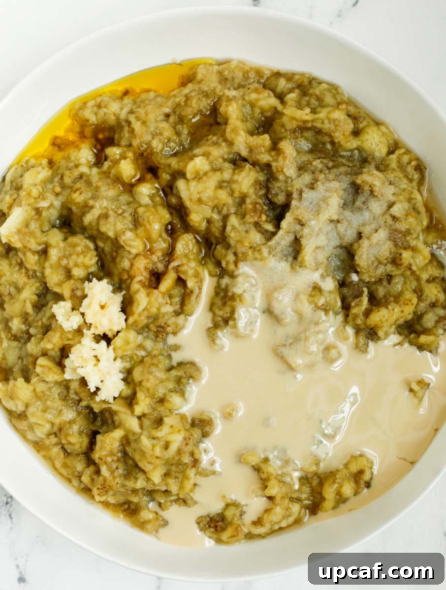 Smoky Lebanese Baba Ganoush 10 A bowl containing finely chopped roasted eggplant mixed with tahini, minced garlic, and other seasonings, demonstrating the hand-mixing process for a chunky Baba Ganoush.