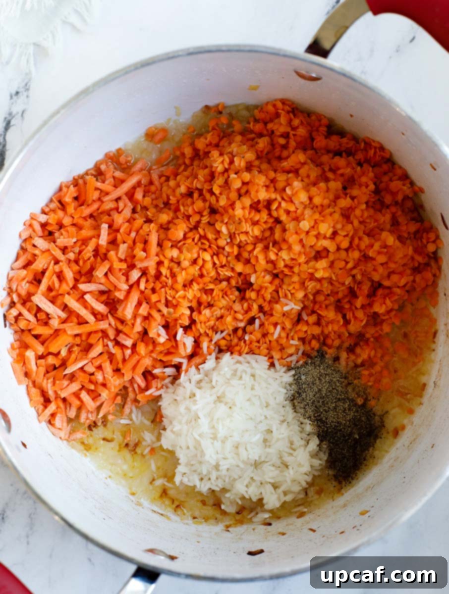 Hearty Lebanese Chicken Lentil Soup 5 Pot containing cooked caramelized onions, along with washed red lentils, shredded carrots, rinsed white rice, cumin powder, and black pepper, ready to be stirred.