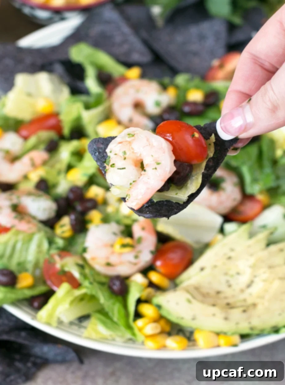 A single bite of Mexican Shrimp Taco Salad on a blue corn tortilla chip held by a woman's hand