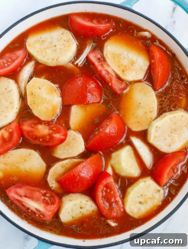 Hearty Kafta and Potato Stew 11 A close-up shot of potatoes and tomatoes simmering gently in a rich, red broth within a pot, steam rising as it cooks.