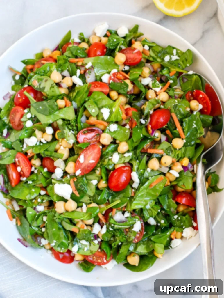 A plate of chickpea and spinach salad, garnished with fresh herbs and a drizzle of dressing.