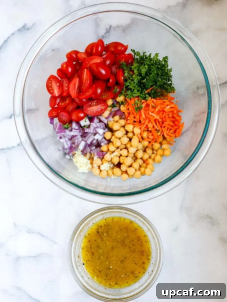 Various fresh ingredients laid out on a table, including baby spinach, chickpeas, grape tomatoes, shredded carrots, parsley, garlic, red onion, and crumbled feta cheese.