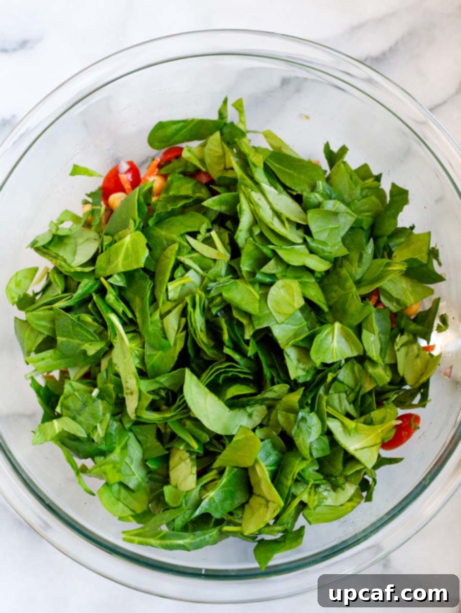Fresh baby spinach being added to a large bowl of colorful salad ingredients.