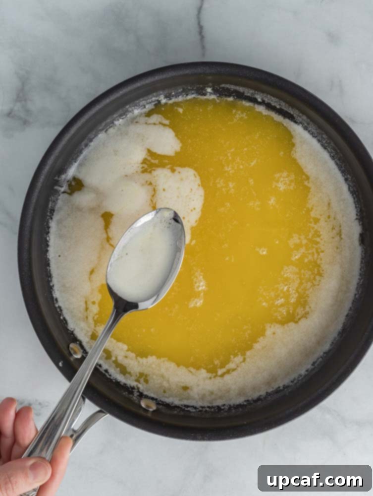 A spoon gently skimming the white milk solids from the surface of simmering butter.