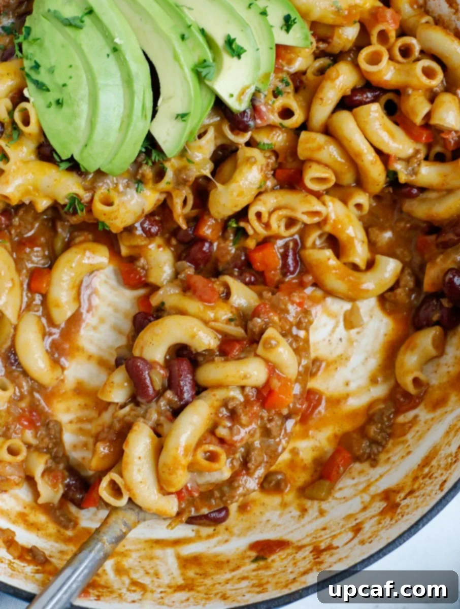 Speedy Cheesy Chili Mac 8 Close up of a pot of chili mac being scooped with a spoon, showing the gooey cheese and rich chili.