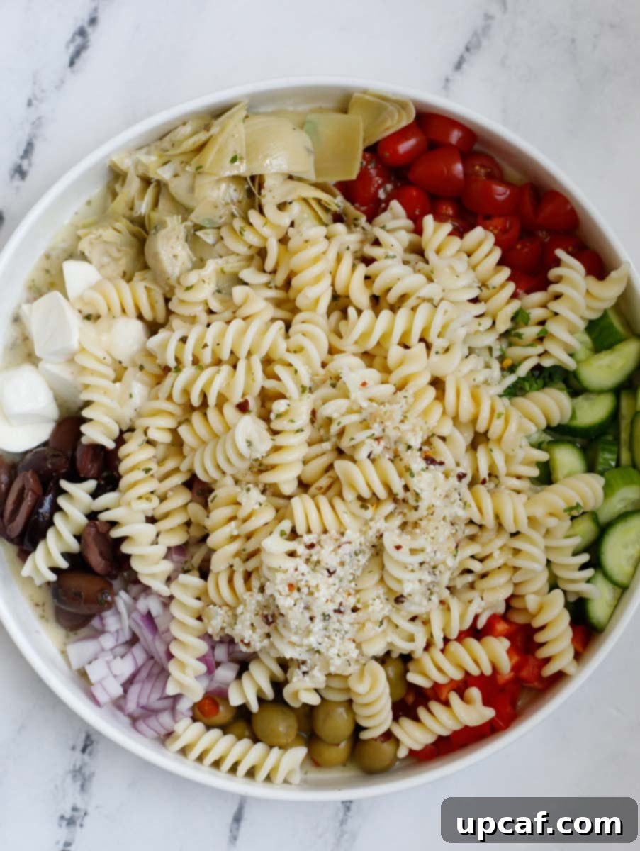 Vibrant Mediterranean Pasta Salad 7 A large bowl with cooled pasta and all the prepared vegetables and cheese, with dressing poured over, before mixing.