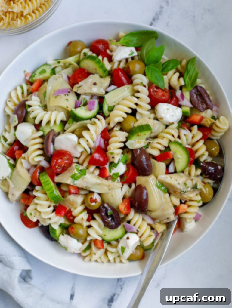 Vibrant Mediterranean Pasta Salad 9 A bowl of Mediterranean pasta salad on a marble surface, with a serving spoon resting in it, ready to be enjoyed.