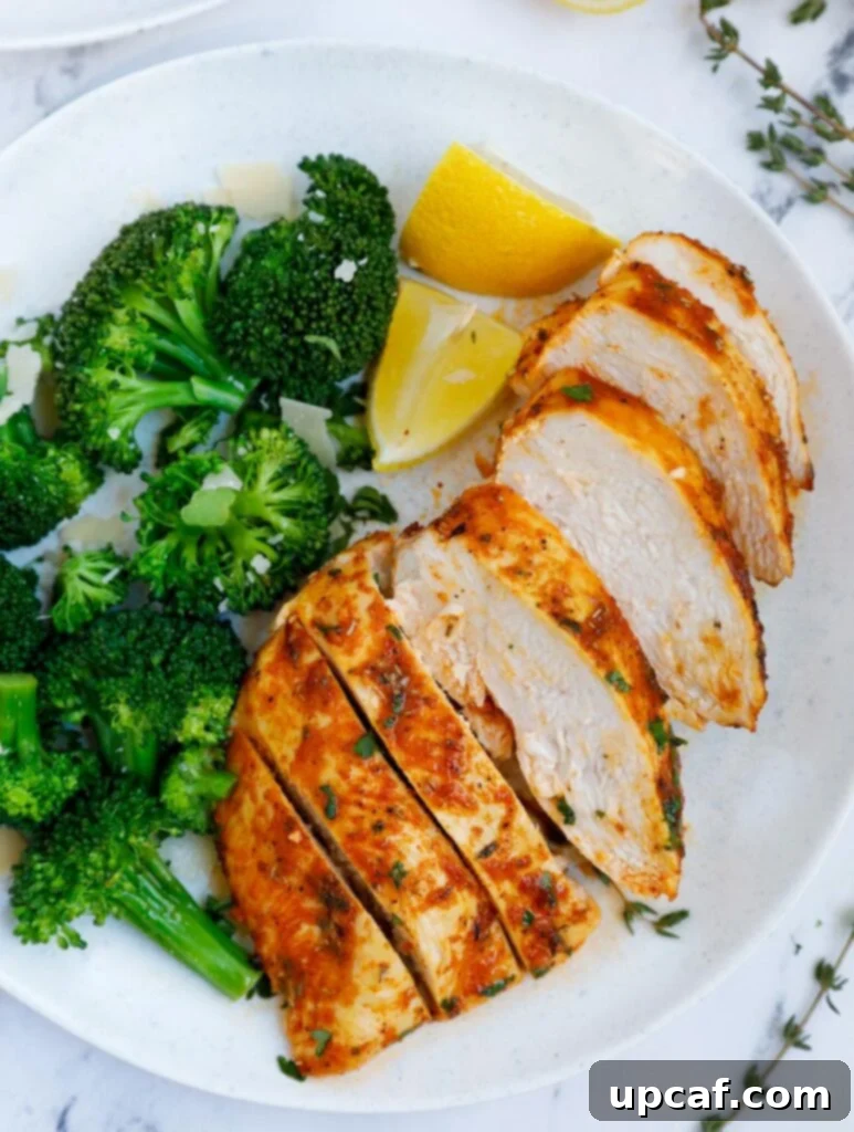 A plate of sliced air fryer rosemary chicken breast beside broccoli.