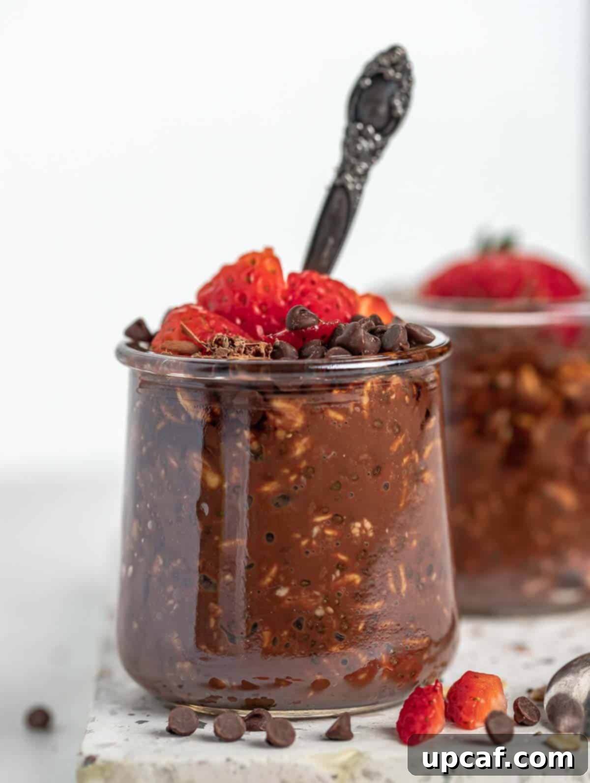 Front close-up view of a glass jar filled with luscious chocolate overnight oats, topped with fresh strawberries and chocolate chips, ready to be enjoyed.