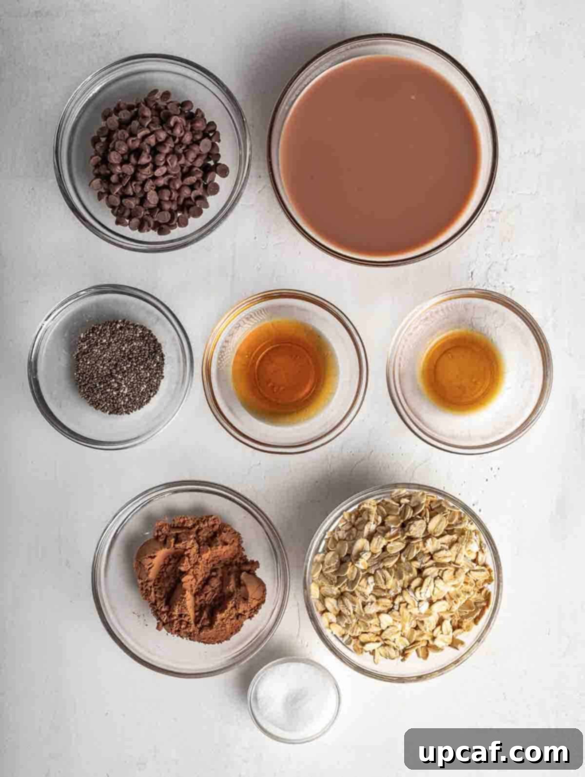 A top-down view of the ingredients for chocolate overnight oats laid out on a kitchen counter, showcasing chocolate milk, oats, cocoa powder, and chia seeds.