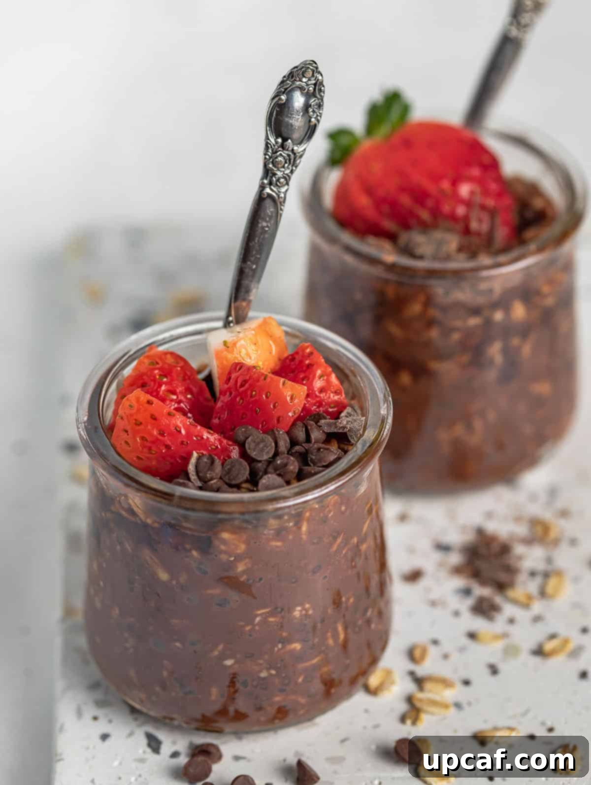 Two glass cups of chocolate overnight oats beautifully topped with fresh strawberries and extra chocolate chips, ready for a delicious breakfast.