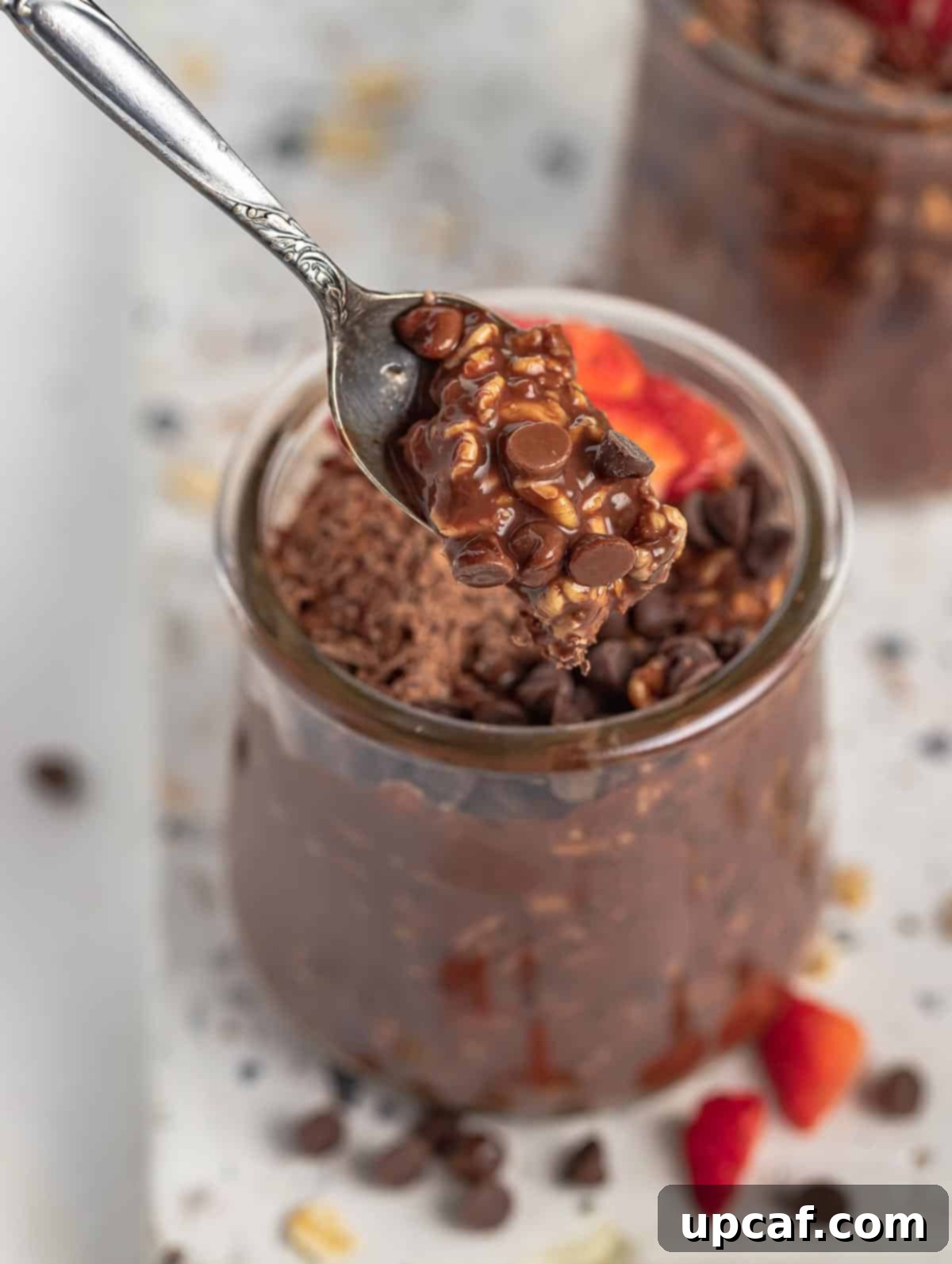 A spoon scooping up a generous portion of creamy chocolate overnight oats from a glass jar, highlighting its rich texture and deliciousness.
