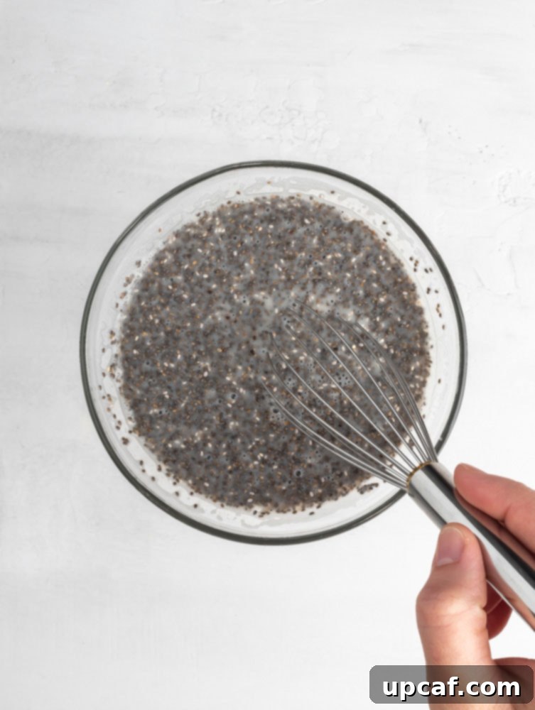 A close-up shot of chia seeds being actively mixed into a bowl with milk and other liquid ingredients, showing the initial stage of preparation for chia pudding.
