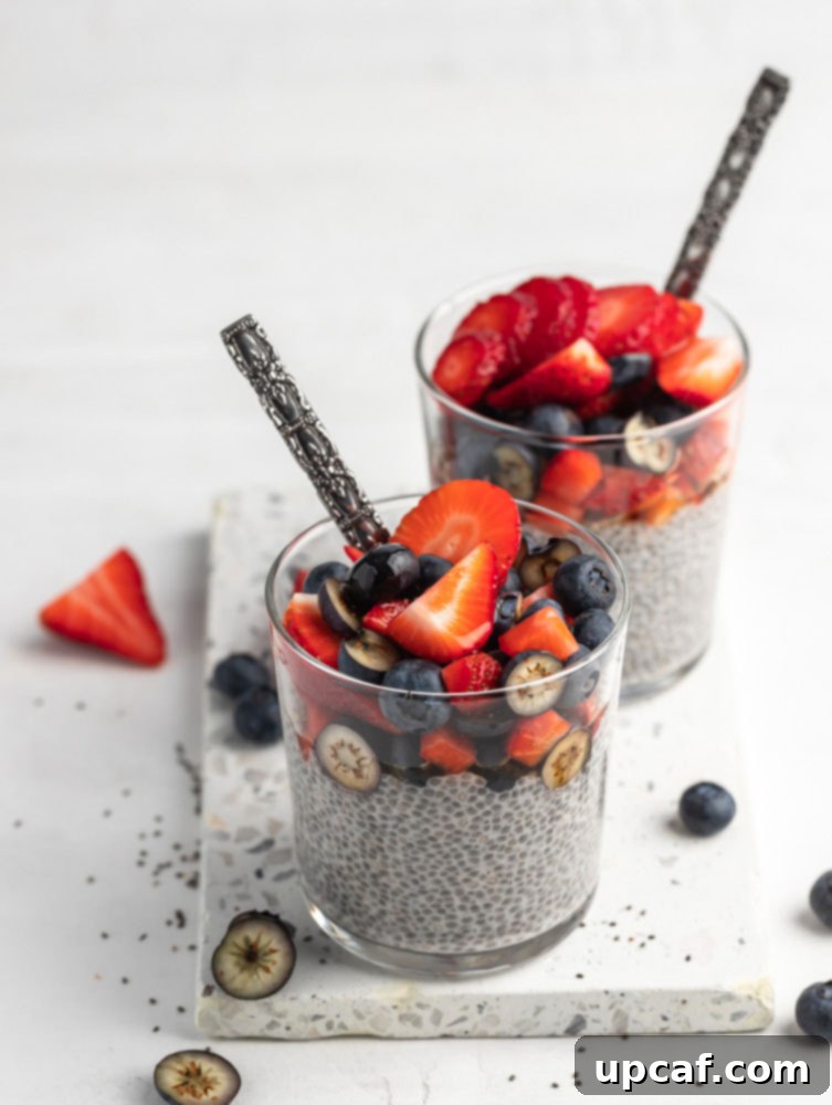 Two beautifully presented chia seed puddings in clear glass cups, artfully topped with a colorful assortment of fresh berries, showing different layers.