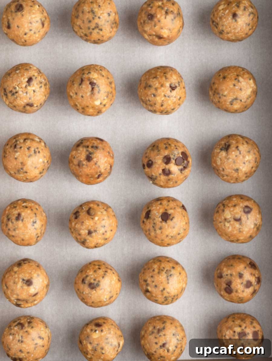 A sheet pan generously covered with parchment paper, holding numerous freshly rolled No-Bake Energy Balls.