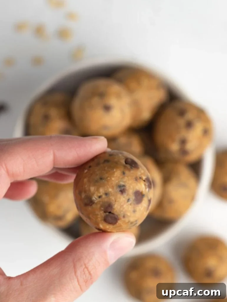 A female hand delicately holding a single No-Bake Energy Ball between two fingers, ready to be enjoyed.