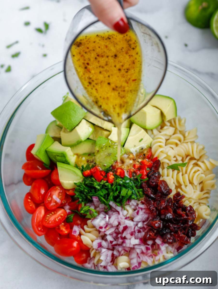 Avocado chicken pasta salad tossed with a zesty dressing in a bowl, showcasing its vibrant colors.
