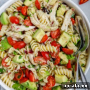 A bowl of avocado chicken pasta salad with a fork and spoon in the bowl.