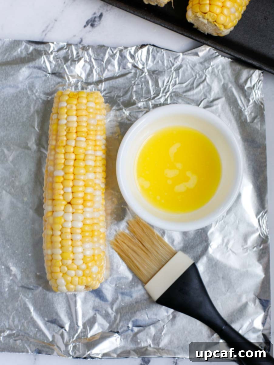 Authentic Mexican Elote 6 Melted butter being brushed onto a corn on the cob wrapped in tin foil.