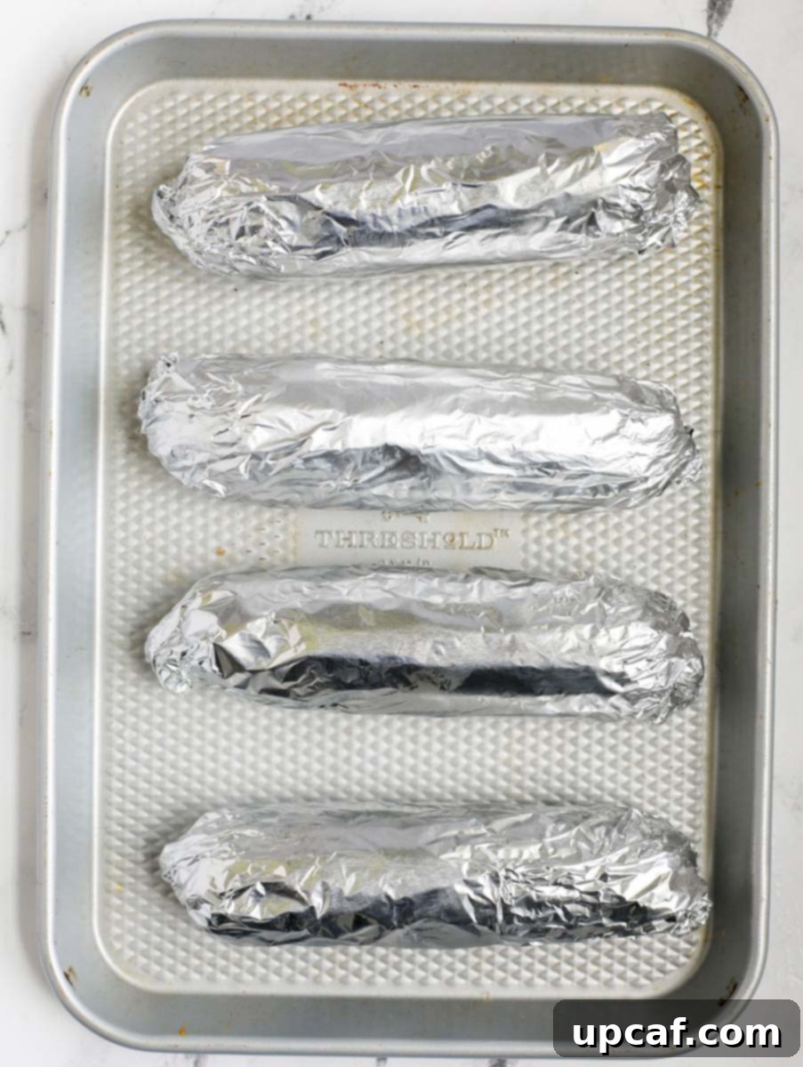 Authentic Mexican Elote 7 Corn cobs, individually wrapped in tin foil, placed on a sheet pan.