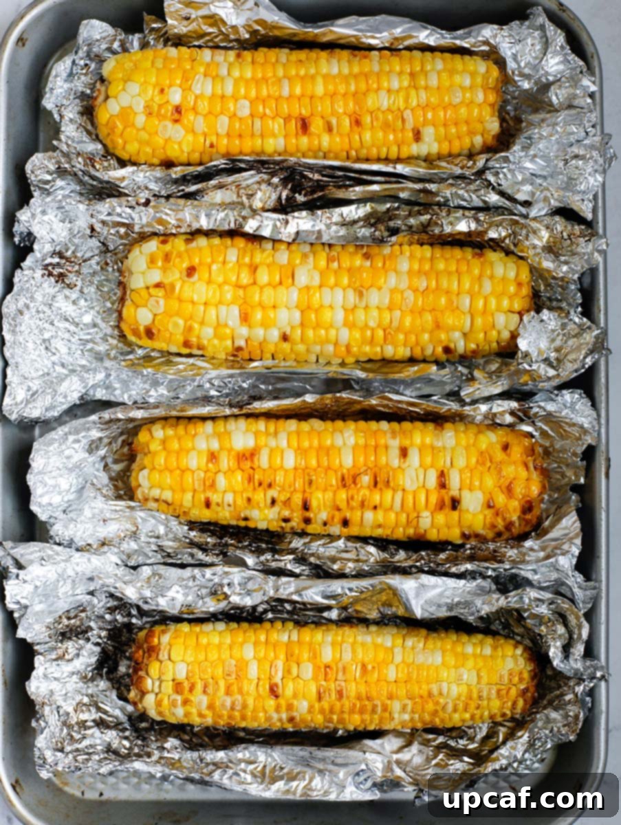 Authentic Mexican Elote 8 Grilled corn, still wrapped in tin foil, resting on a sheet pan after cooking.