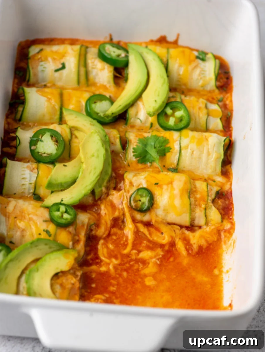 Southwest Chicken Zucchini Enchiladas 7 Baked chicken zucchini enchiladas in a baking dish, with a few pieces removed to show the interior and texture.