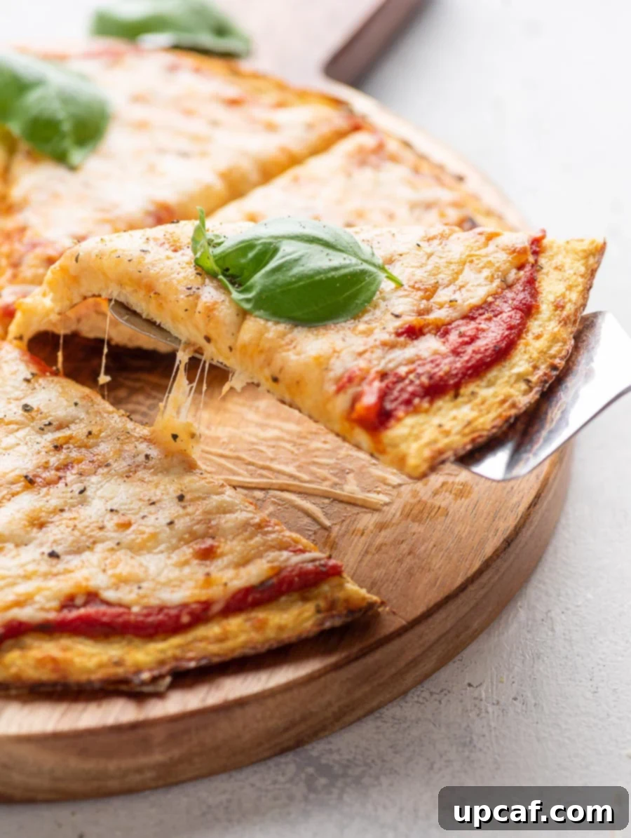 A slice of cauliflower pizza being lifted from the whole pizza with a spatula, showing the golden crust and melted cheese.