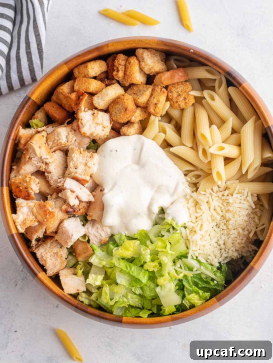 ingredients of chicken caesar pasta salad in a wooden bowl