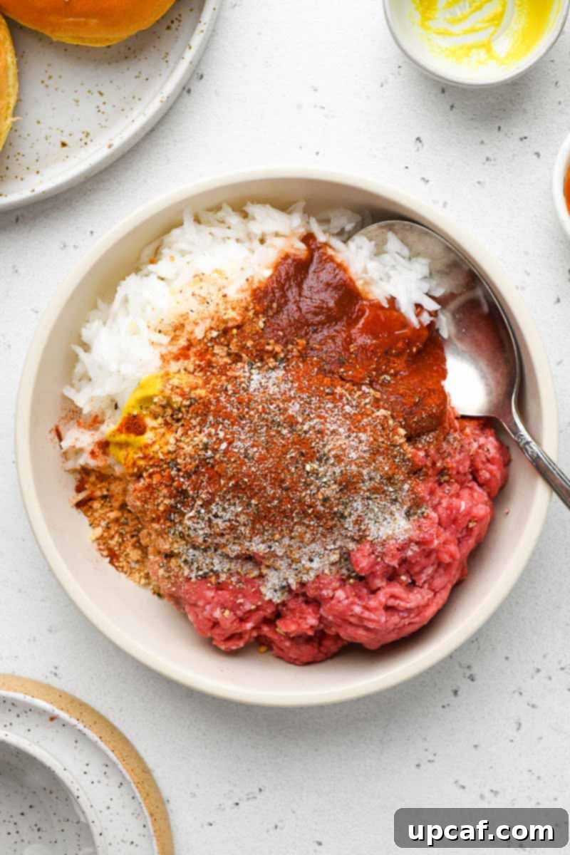 A large mixing bowl containing ground beef and all the seasonings and ingredients, partially mixed together, ready for patty formation.