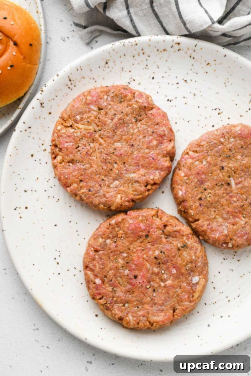 Three perfectly shaped raw beef burger patties resting on a plate, ready for grilling.