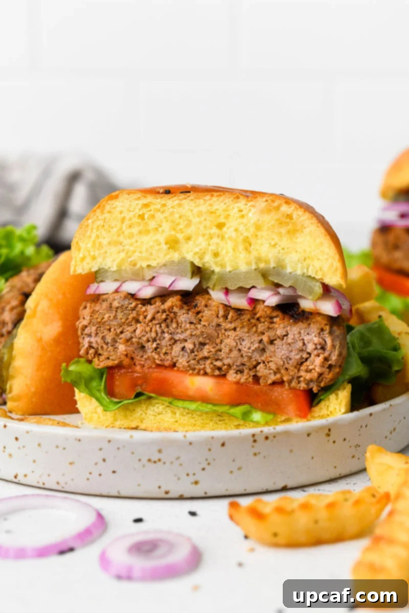 A gourmet homemade beef burger, cut in half to reveal its juicy interior and melted cheese, served on a plate with crispy onion rings and a refreshing drink.