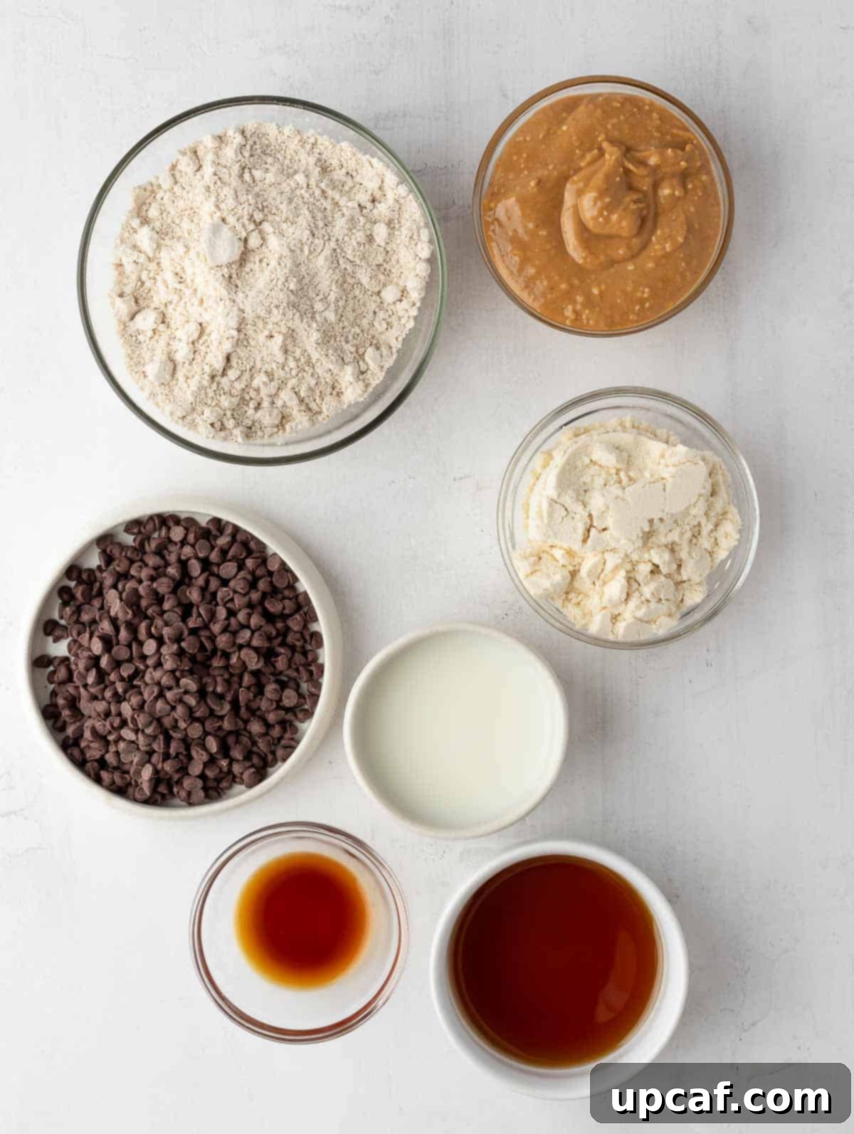 A vibrant flat lay of all the essential ingredients for making protein cookie dough balls, including oat flour, protein powder, chocolate chips, and peanut butter.