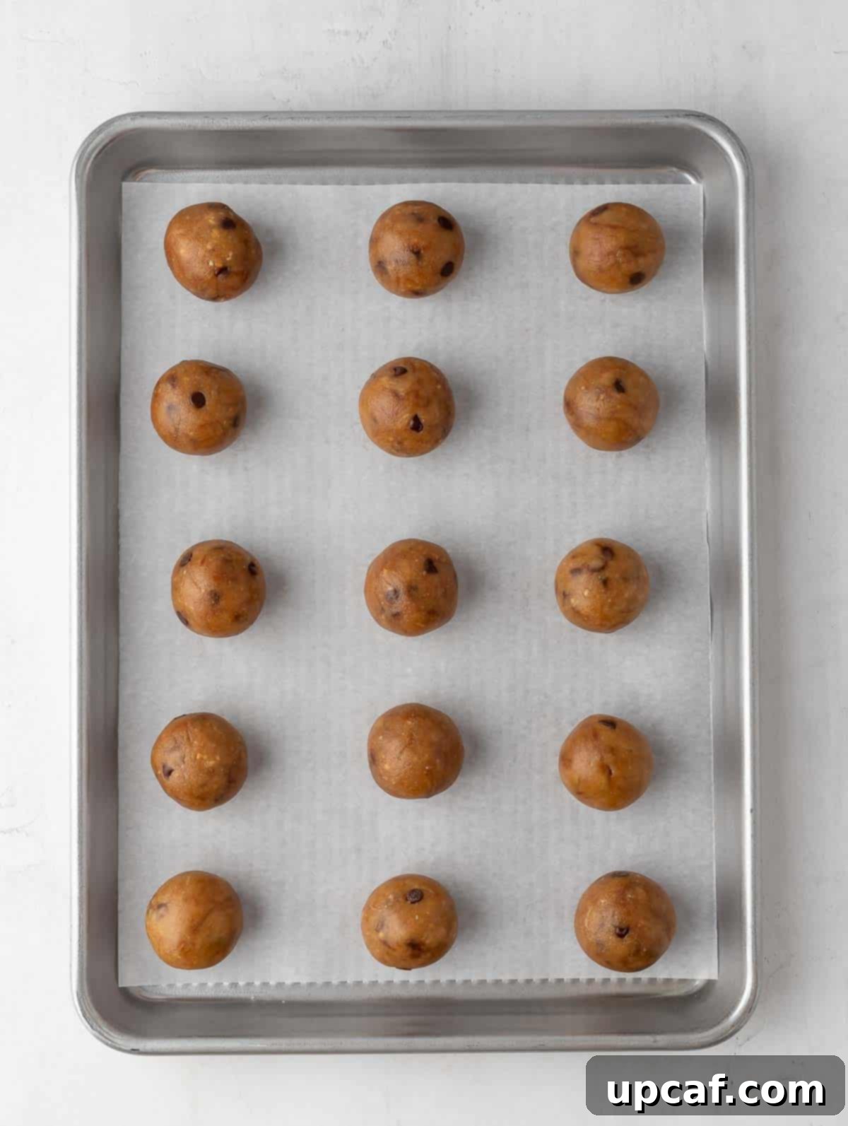 Freshly rolled protein cookie dough balls neatly lined up on a sheet pan covered with parchment paper, ready for chilling.