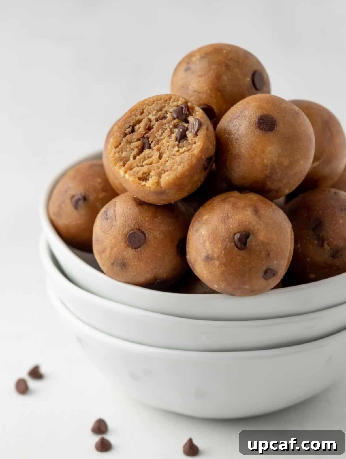 Close-up of protein cookie dough balls in a white bowl, with one ball having a bite taken out, revealing its rich, textured interior.